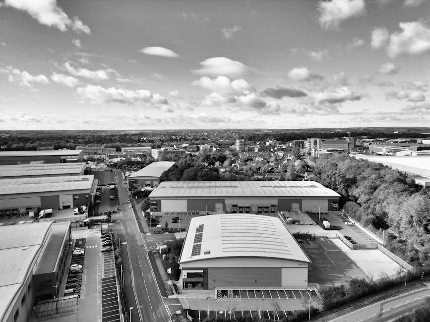 An aerial black-and-white photograph showing a commercial industrial area with multiple warehouse-style buildings featuring flat roofs, some of which have solar panels installed. The buildings are pos